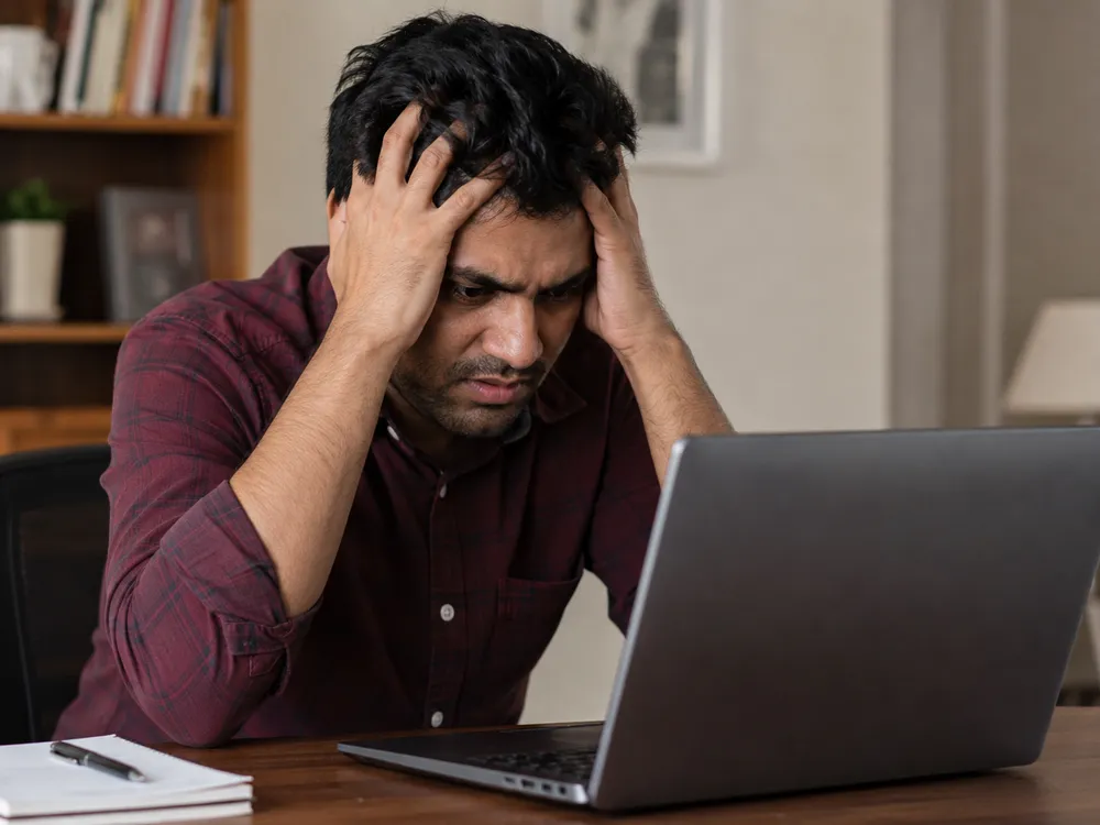 Indian man looking stressed while checking a laptop after an online deposit problem